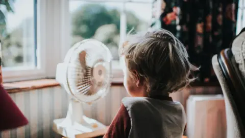 Getty Images A photo of child in front of a window and an electric fan