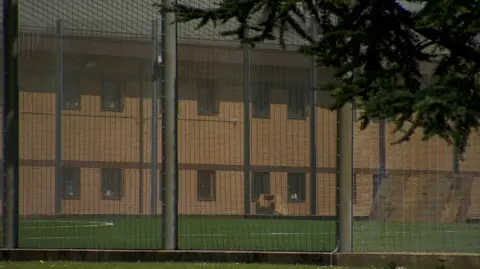 A view of one wing of HMP Hindley through the railings surrounding an artificial turf football pitch. 