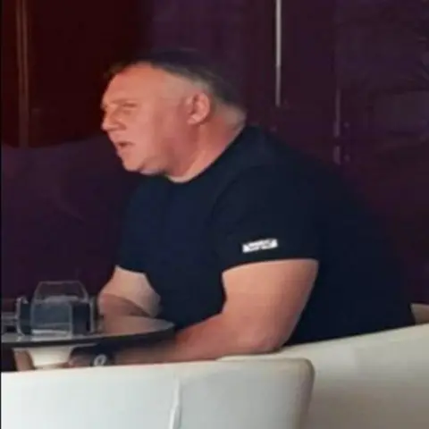 Police Scotland Jamie Stevenson sitting on a white chair in a hotel, with a table in fromt of him. He is weering a black tshirt