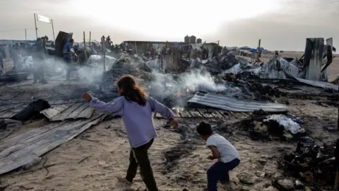 EPA Palestinians inspect the damage after an Israeli army raid on a camp at an area designated for displaced people in Rafah, southern Gaza Strip.
