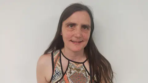 Alison Manning has long dark hair and is wearing a strappy dress with batik-type panels in brown and orange