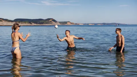 Getty Images Teenagers enjoying the seaside in Dorset, United Kingdom. They are playing with a small ball while standing in the sea.