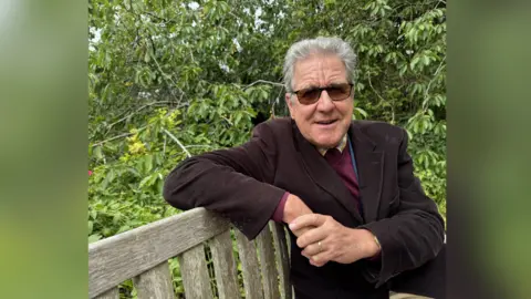 Jo Burn/BBC Canterbury Historical Association chairman Julian Waltho sat on a bench at Canterbury Cemetery.