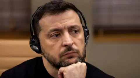 Zelensky wearing headphones and looking pensive with his head resting on his hand