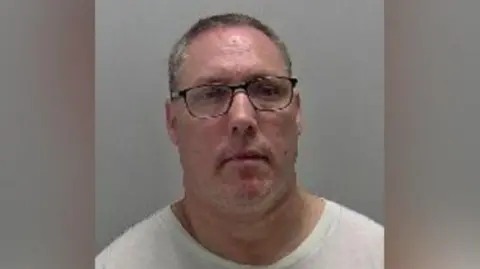 Warwickshire Police A mugshot of Scott Dobson-Smith wearing dark glasses and a white t-shirt with a grey background