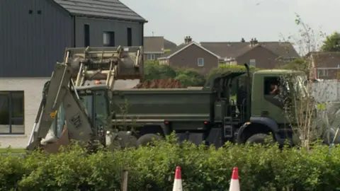 Excavator loads sand into a flatbed truck in the Rivenwood residential area 