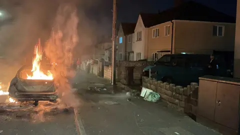 PA Media A car set alight in Ely during disorder in May 2023