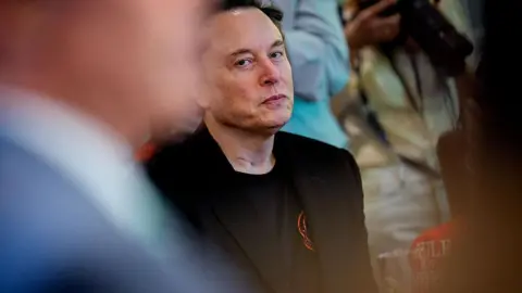Elon Musk peers over at another person, looking unimpressed