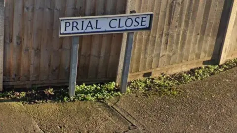 A close-up of the street sign for Prial Close in Lincoln. The sign is fixed to two concrete posts with a shiplap-style fence in the background.