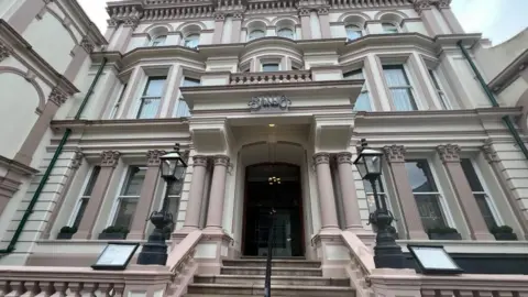 The photo looks up at a three-storey building from the bottom of the steps to the main entrance. The sign above the main doors says the restaurant's name, Banjo. The building is painted in cream and dull pink colours, with four large pillars around the main entrance. 