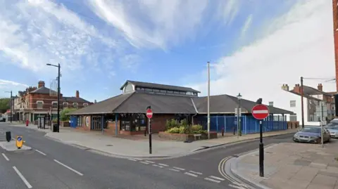 Google view of the current library on Alexandra Road by Pier Gardens. It has blue metal railings and a glass skylight on its roof.