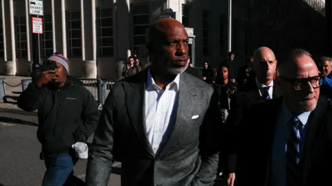 REUTERS/Adam Gray Chauncey Billups is on a sunny street outside wearing a suit and shirt. He has a somber expression and appears to be walking and looking to his left., He is surrounded by people. 