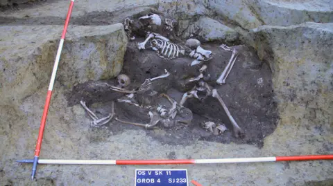 Novak et al Several skeletons lying in sand and rocks in the archaeological dig.
