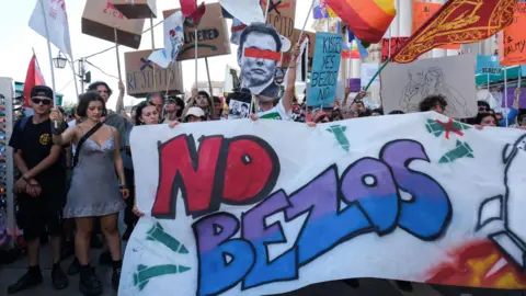 Reuters Protesters in Venice holding a sign that reads "No Bezos" in spray paint, banners and a printed photo of Elon Musk
