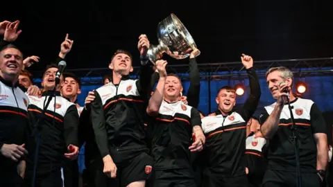 Getty Images Armagh players celebrate on stage at the homecoming event on Sunday. Their manager  Kieran McGeeney smiles as the players celebrate with the cup.