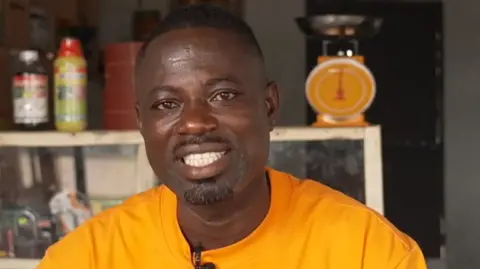 A head and shoulders image of Emmanuel Asamoah. He is smiling and wearing a bright yellow top.
