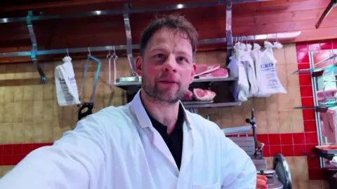 Chris McHugh/BBC Butcher Sam Vine posing for an image at Griffins Family Butchers. Some meat can be seen behind him.
