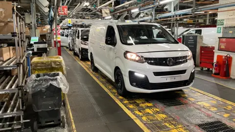 Sam Read/BBC A white van on the production line at the Vauxhall plant in Luton, with several other vans behind and shelving alongside