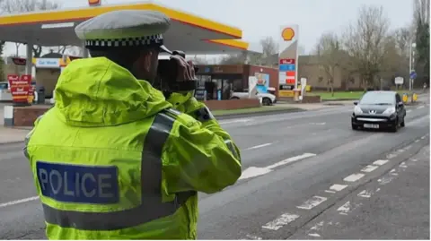 A police officer is carrying out a roadside speed check on an approaching vehicle