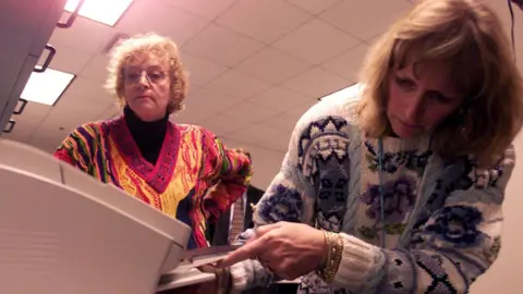Getty Images Two women in Palm Beach, USA, bend over a fax machine as one tries to clear a paper jam