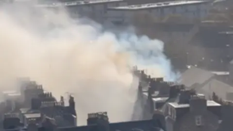 Smoke billowing rooftops in Aberdeen city centre, the sea and a lighthouse can be seen in the distance.
