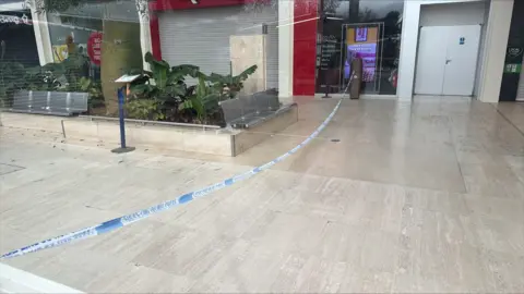 Richard Knights/BBC A long piece of blue and white police tape stretches across the concourse inside Centre MK. It is next to a set of seats.