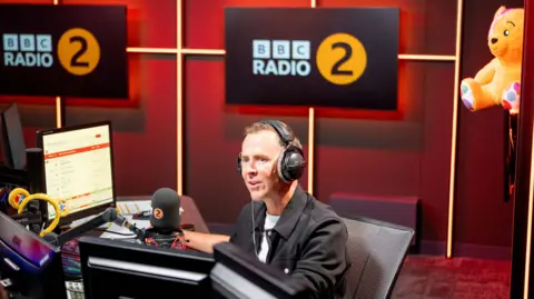 Scott Mills wearing a black jacket in the BBC Radio 2 studio