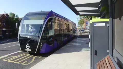 A purple Glider vehicle at a passenger halt in Belfast