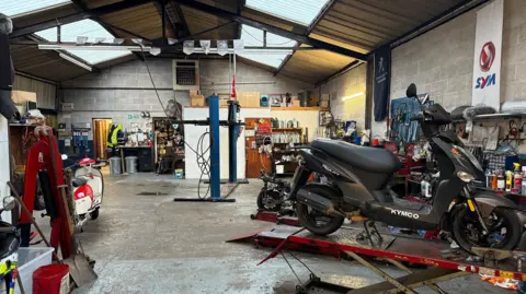 The inside of the Anderson & Wall workshop. There is a motorbike on a ramp and many tools around the space.