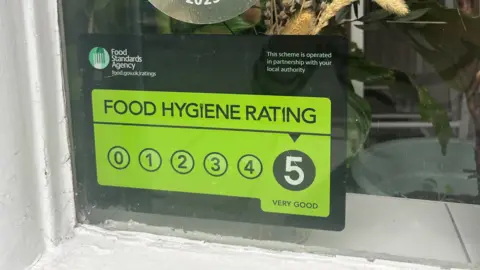 Food hygiene rating sticker in a store window showing a five out of five rating