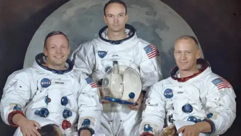 Retrato oficial de la NASA de la tripulación del Apolo 11 Neil Armstrong, Michael Collins y Buzz Aldrin, vestidos con sus trajes de espacios, tomados en el telón de fondo de una imagen de la luna