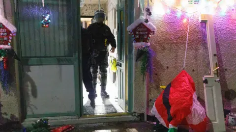 GMP A police officer dressed all in black can be seen walking out a property decked in Christmas decorations. 