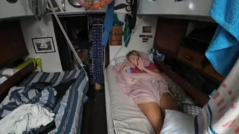 Rob Donald The interior of a small yacht, a teenage girl waves at the camera from her bunk 