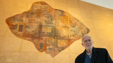Palestinian Museum Sliman Mansour stands in front of his artwork, On the Wing of an Angel, Part of the Palestinian Museum Permanent Collection, in Birzeit, in the occupied West Bank