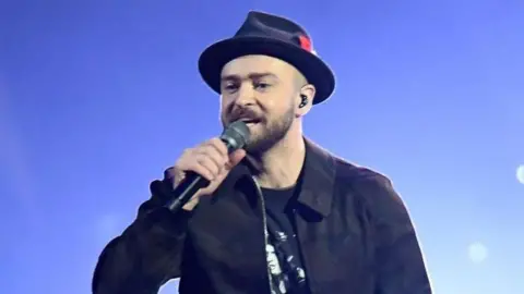 PA Media Justin Timberlake performing on stage. He is wearing a black hat, jacket and trousers.