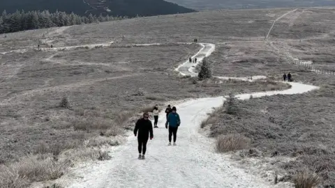 People walking a mountain path in Gortin, County Tyrone. Light snow is on the path and mountains.