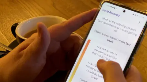 Person holding a phone showing the NHS Long Covid clinic app