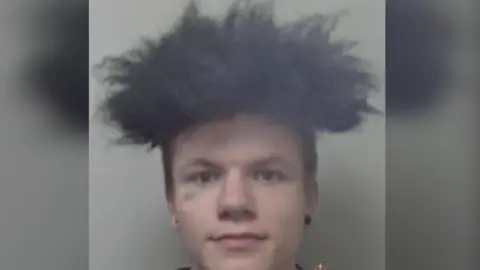 Kent Police A man dark hair and wearing black studs.