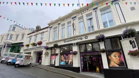 The Nelson Place building on Smith Street in St Peter Port is predominantly painted white with black painted trim and a black Superdrug logo above the floor way of the building.