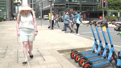 BBC Karishma Shah walking past e-scooters