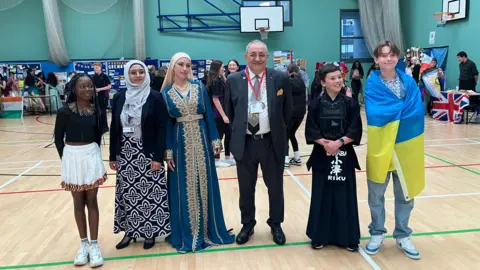 Shariqua Ahmed /BBC Marco Cereste dressed in a suit alongside Sidra Hussain and some of the students taking part in the event
