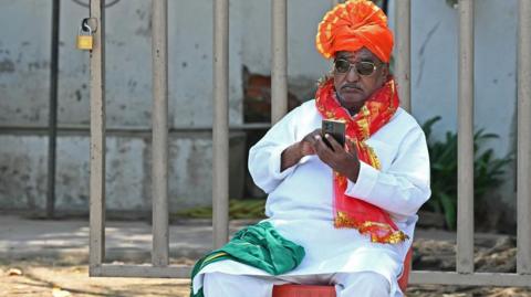 A supporter of Bharatiya Janata Party (BJP) uses his mobile phone before a roadshow by BJP candidate ahead of the second phase of voting for country's general elections, in Hyderabad on April 24