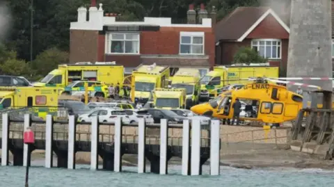 EDDIE MITCHELL ambulances and a helicopter lined up by the shore
