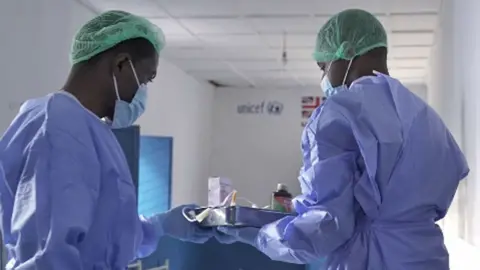 Unicef Healthcare workers in blue PPE holding a tray of medicine at Goma's Mugunga health centre