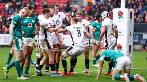 Getty Images England A players in their white kits celebrate a try against Ireland A at Ashton Gate. The stands with some spectators in can be seen in the background