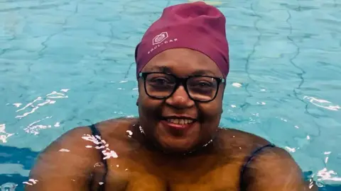 Jaunita Mayers wearing a purple swim cap and smiling at the camera from the pool