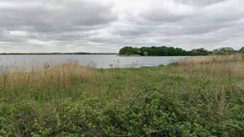 Google A Google Streetview of a lake with greenery in the foreground.