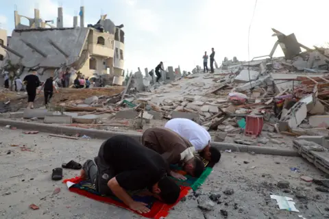 Majdi Fathi / Getty Images Muslim men perform the morning Eid Al-Fitr prayer with destroyed buildings behind them in Beit Lahia in the northern Gaza Strip