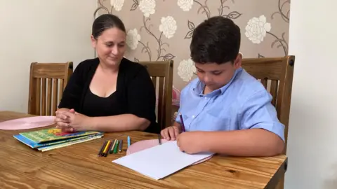 Samantha Rodger-Smith sitting at a table with her son Finley, who is drawing on paper