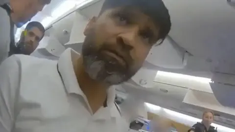 Surrey Police Police footage of Urfan Sharif in a white polo on a plane.